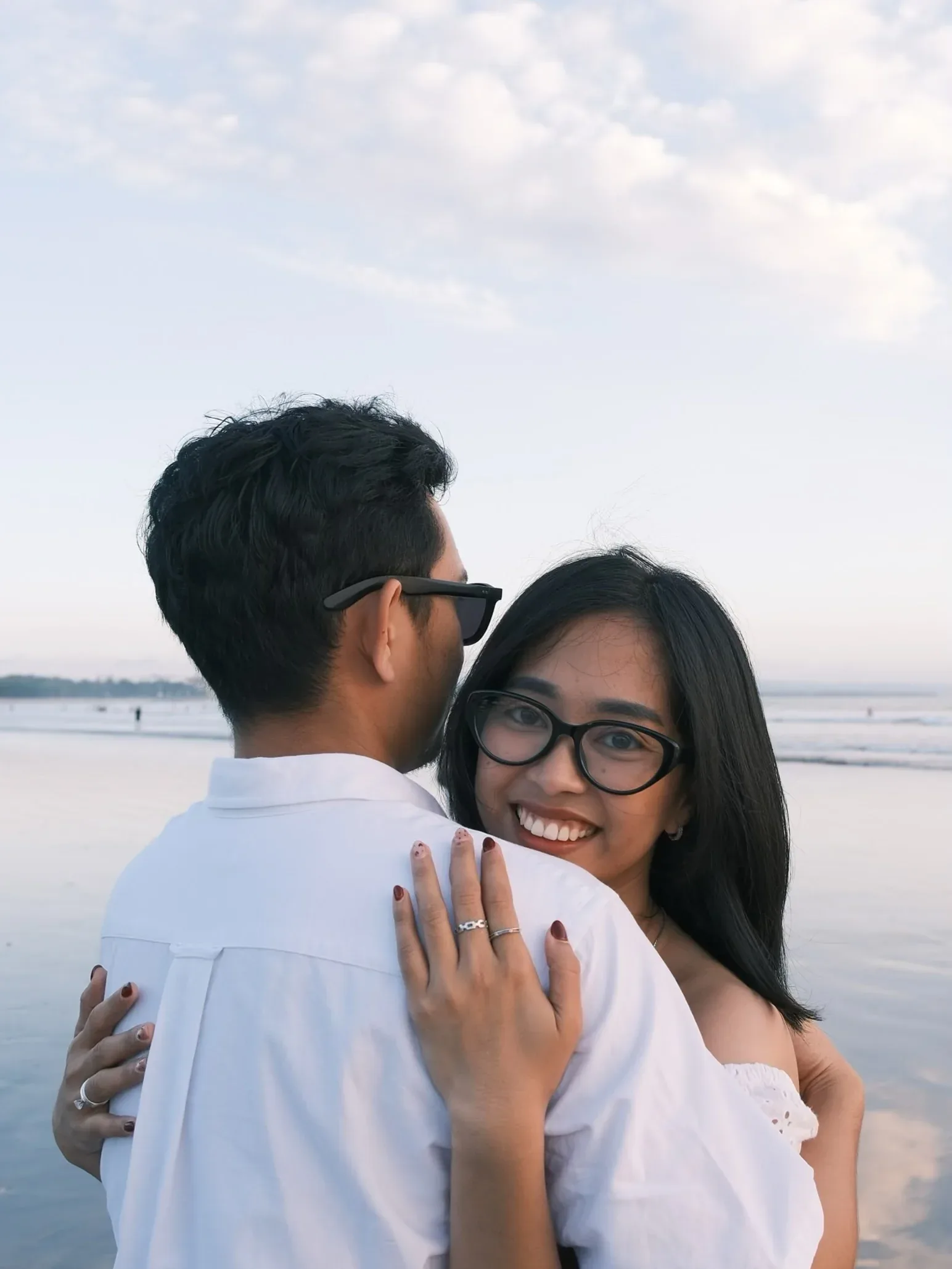 Her holding him and looking back over his shoulder at the camera, the sea flat behind them.